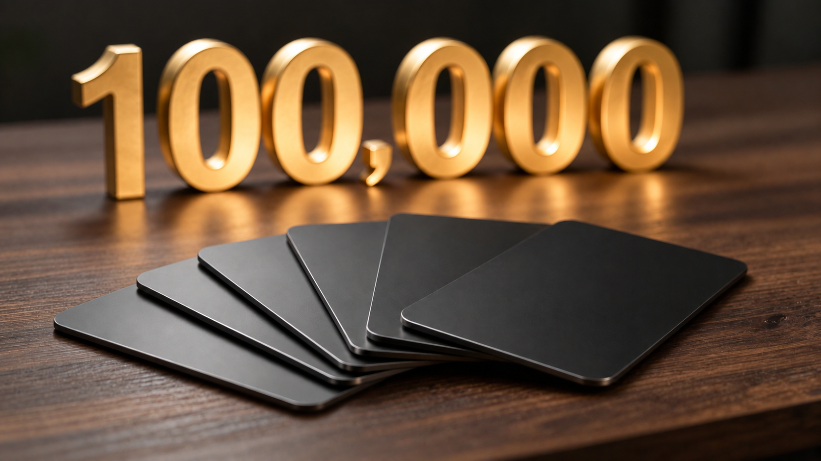 Blank dark credit cards fanned out on a wooden desk beneath gold numerals reading 100,000.